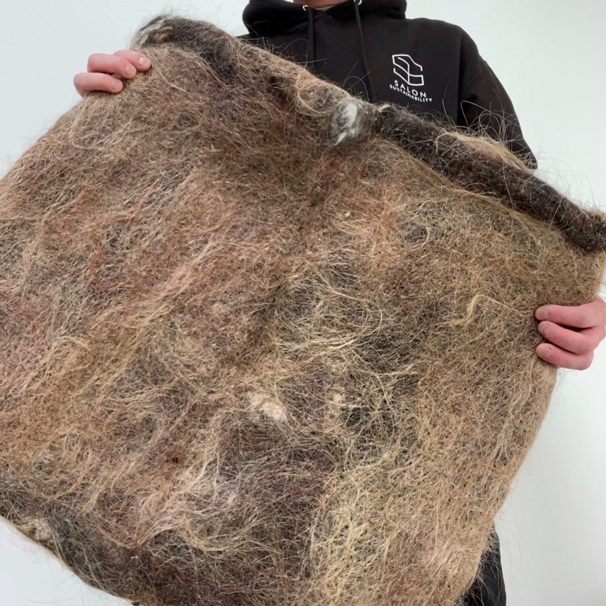 A person holding a mat made from hair fibres
